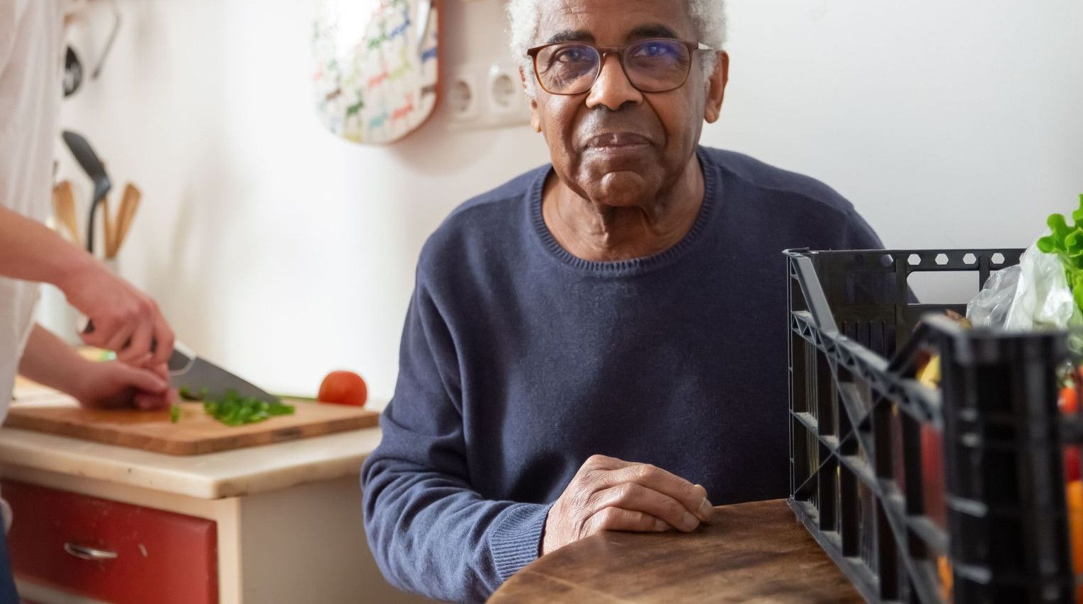 A young adult helping a senior in the kitchen, highlighting care and support at home.